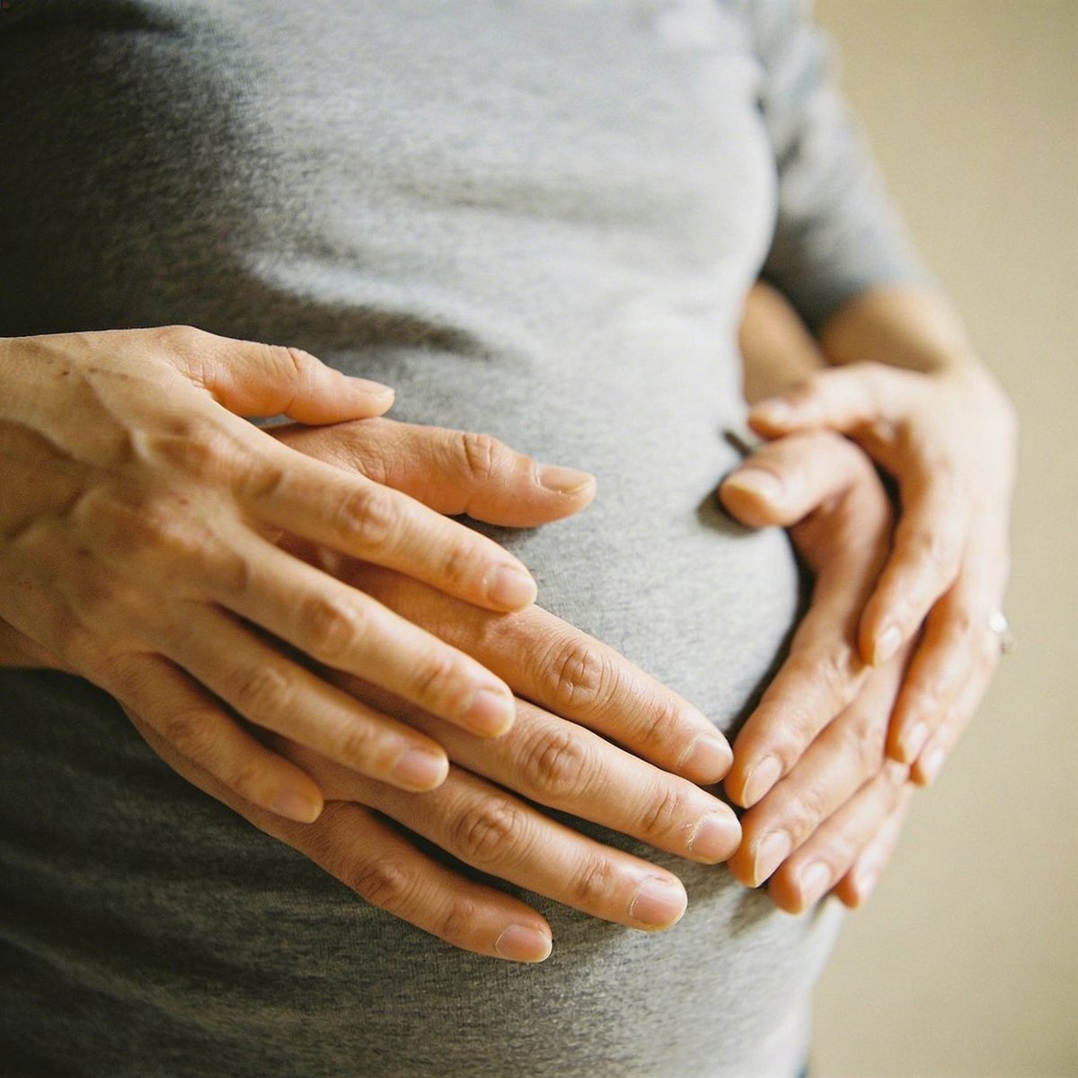 Grande plano das mãos em forma de coração sobre a barriga redonda